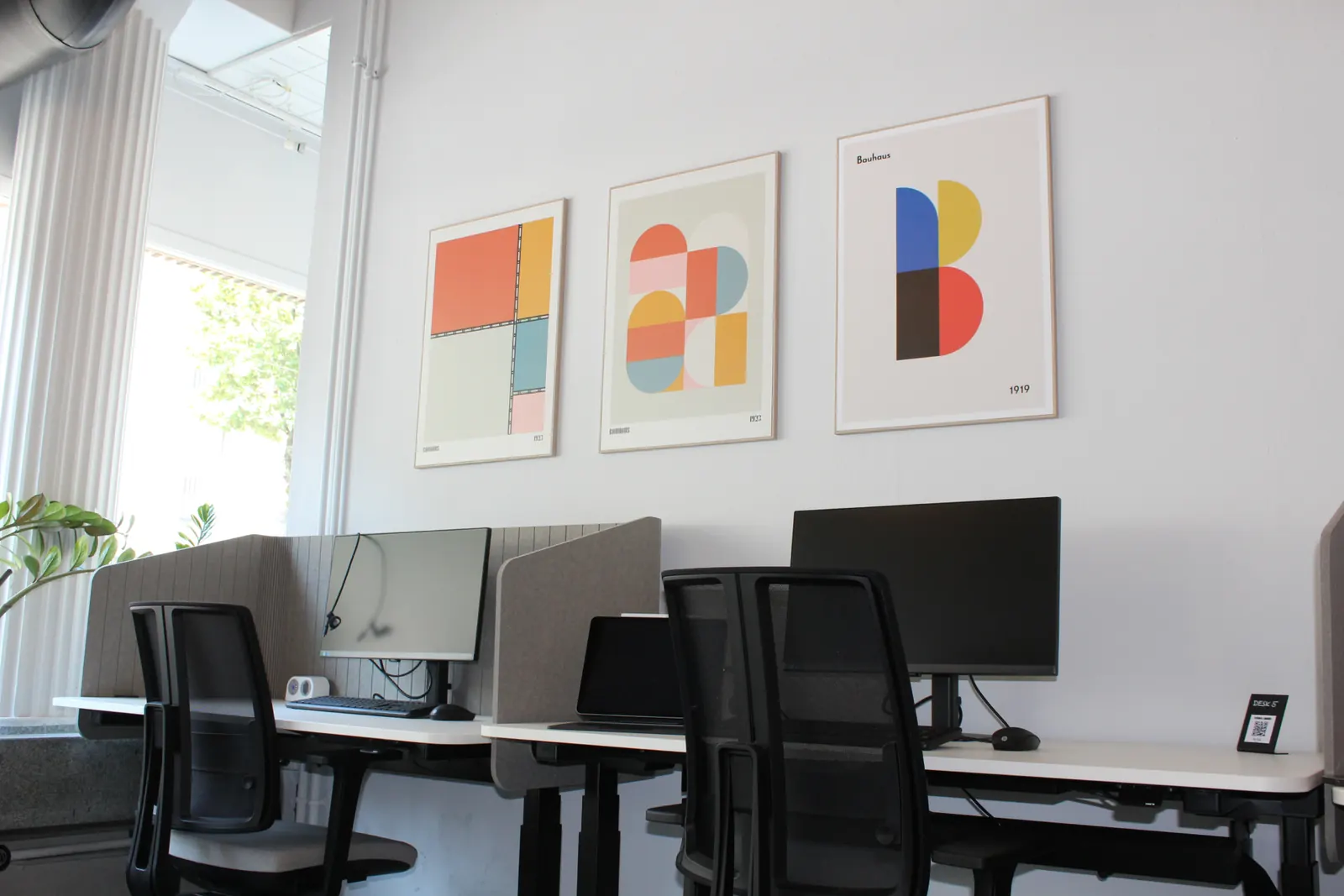 Arbeitsplätze mit Monitoren in der Open Zone von the desk, darüber drei farbige Bauhaus-Poster